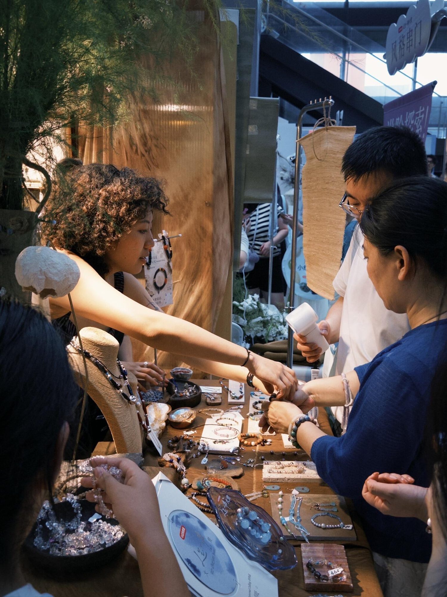 Jewelry maker and visitors discussing handmade jewelry at a market stall