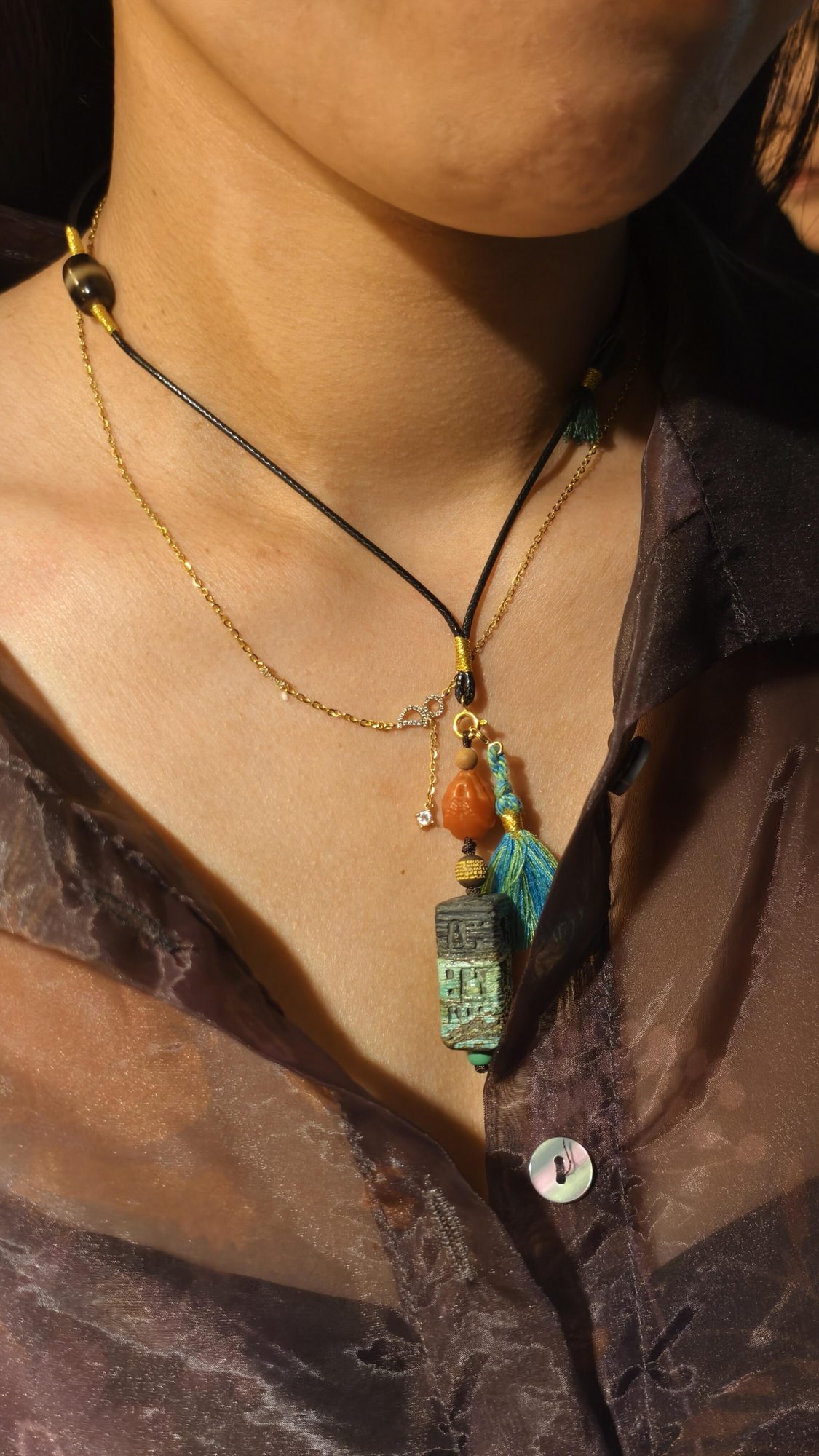 Layered handmade pendant necklaces worn over a brown shirt