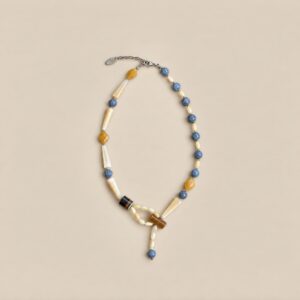 Full view of an asymmetrical natural stone and shell necklace with blue beads, yellow accents and an extension chain.