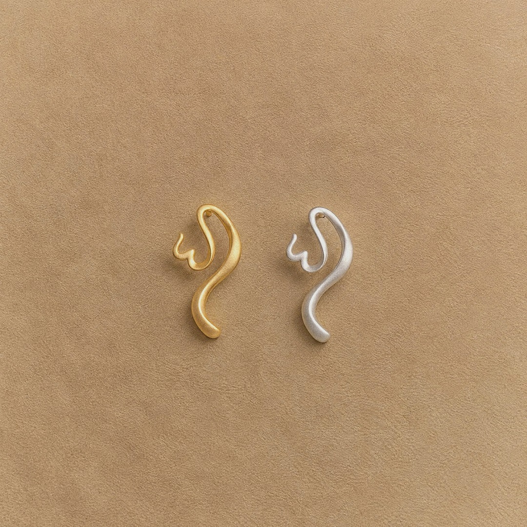 One gold-plated and one platinum-plated sterling silver earring with flowing calligraphic curves on a beige background.