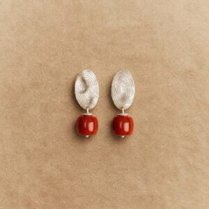 Pair of red Nanhong agate drop earrings with oval fingerprint-like platinum-plated copper tops on a beige background.